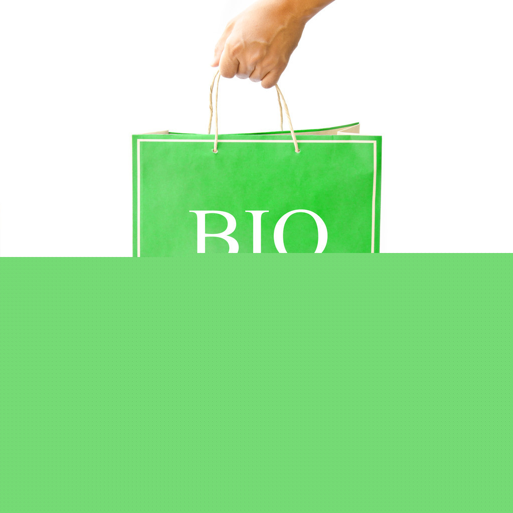 手保持绿色的纸购物袋上反映出白色的地板